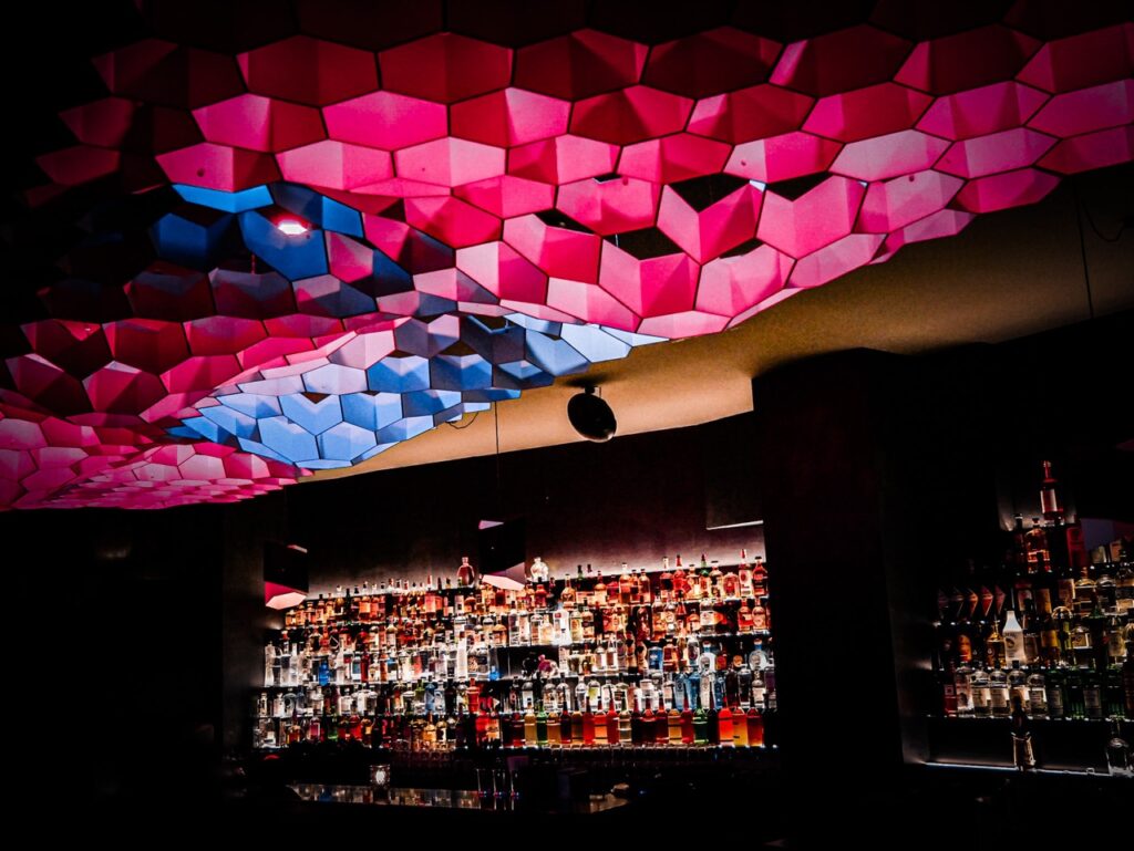 A refreshing cocktail served on a bar coaster at Sharlie Cheen Bar in Berlin Mitte, illuminated by ambient lighting with shadow patterns.